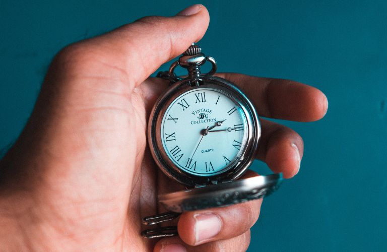 analog pocket watch held in a hand with a bluish green background