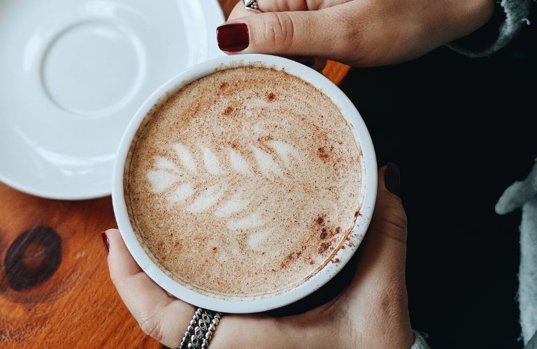 latte art with cinnamon held between two hands with painted fingernails