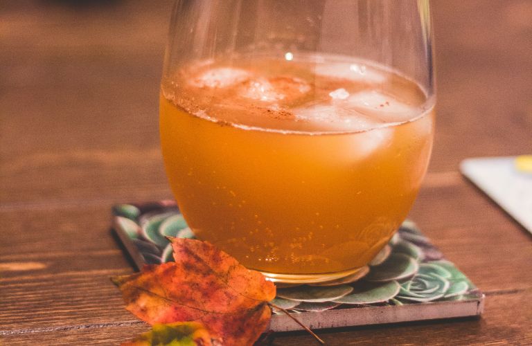 apple cider on a decorative coaster next to an autumn leaf