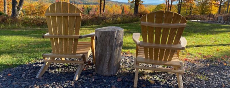 two wood lawn chairs on rocks in a back yard facing a scenic vista