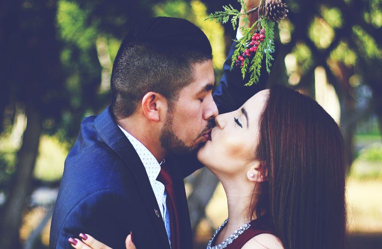 a couple kissing while mistletoe is held above and between them