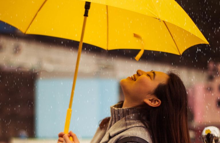 woman holding an umbrella looking up as it rains