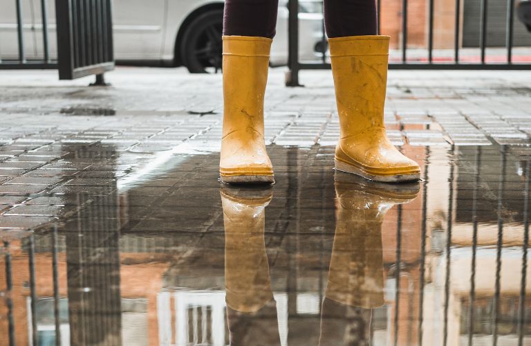 person standing in a puddle after the rain wearing yellow rain boots looking at their reflection