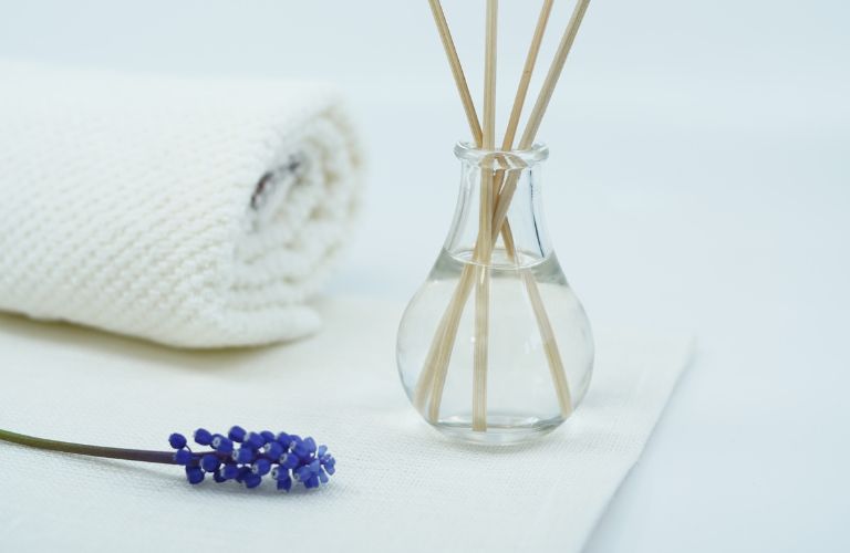scented oil diffuser, towel and sprig of lavender set up together on a bathroom countertop